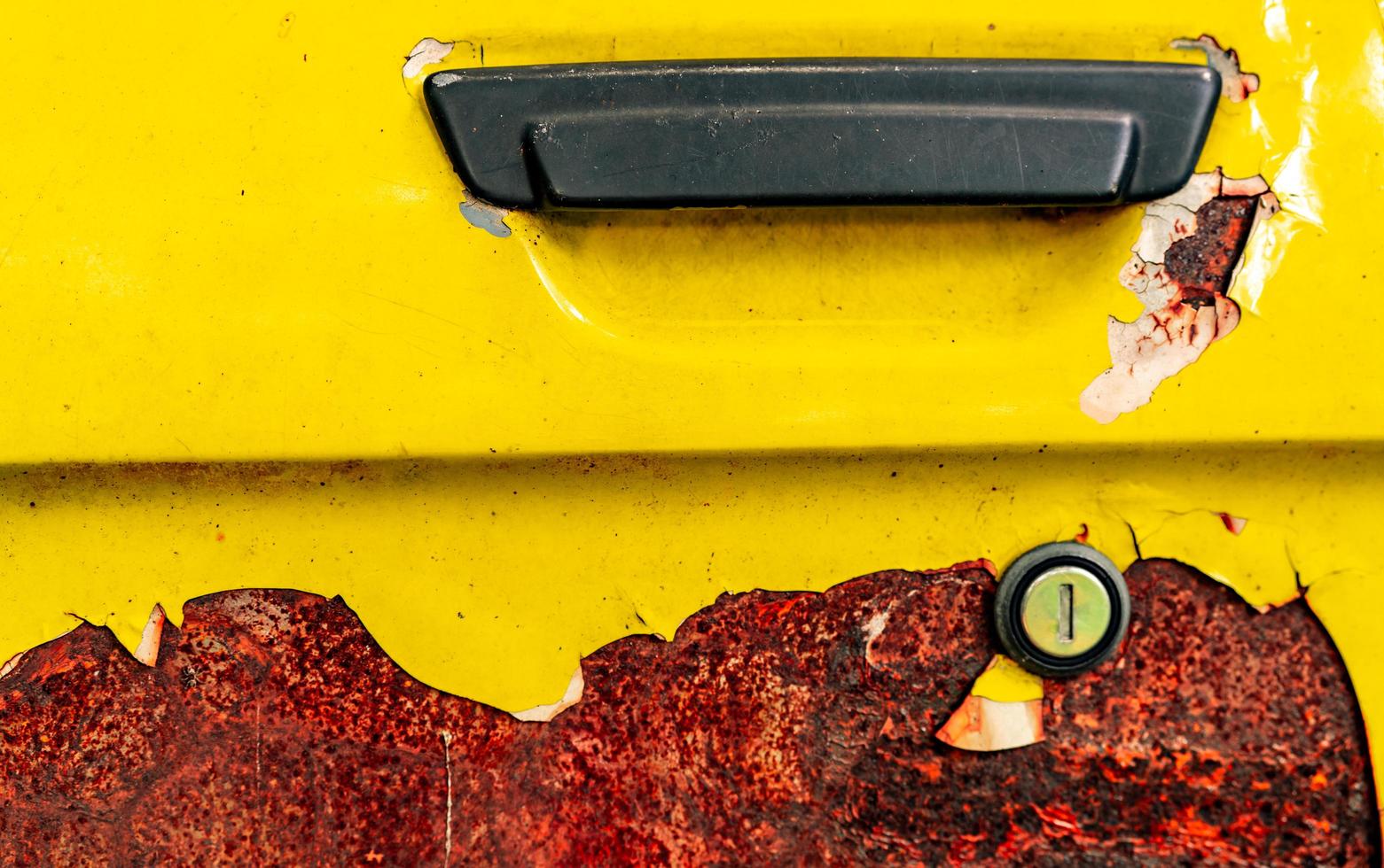 close-up oude autodeur met roestig. verlaten roestige gele auto met zwart handvat. auto kleuring is peeling. oude en verroeste auto deur textuur achtergrond. gebarsten verf. gat van autosleutel. foto