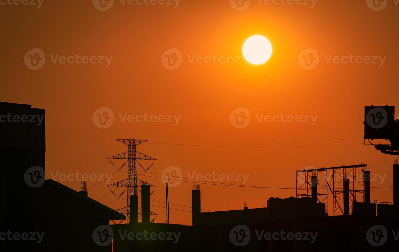 silhouet bouwplaats met oranje zonsondergang hemelachtergrond. hoogspanning elektrische toren. mooie grote zon bij zonsondergang in de stad. dramatische hemel in de schemering. steigers op bouwplaats voor huisvesting foto