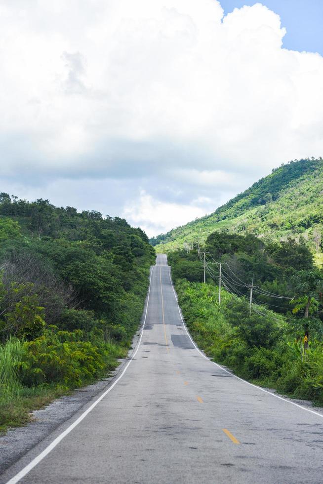 weg naar berg - een lange rechte weg die leidt naar een groene natuurboom op de bergen, asfaltweg in thailand foto