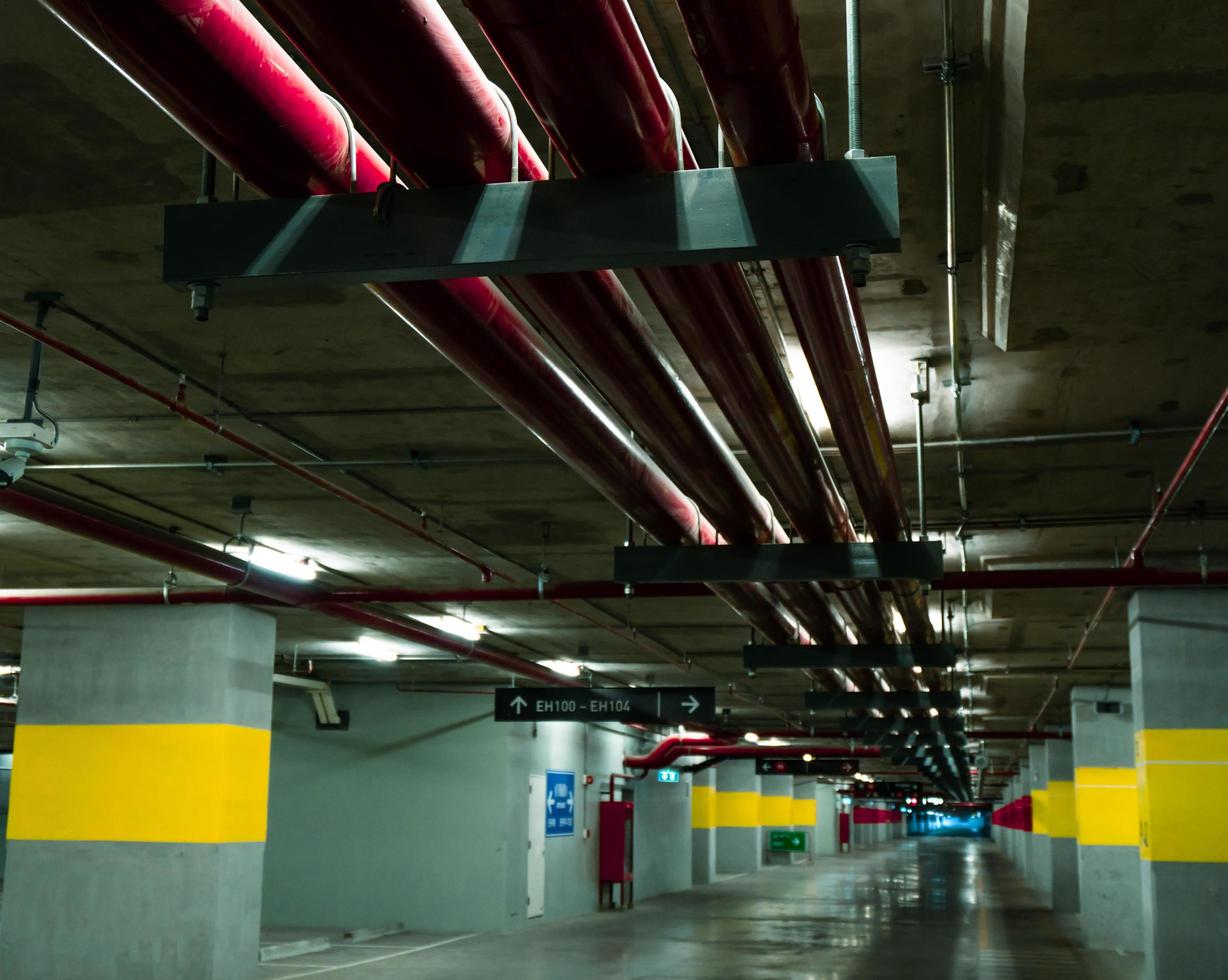 perspectief van lege overdekte parkeerplaats in het winkelcentrum. ondergrondse betonnen parkeergarage met open lamp 's nachts. bedrading en sanitair in het winkelcentrum foto