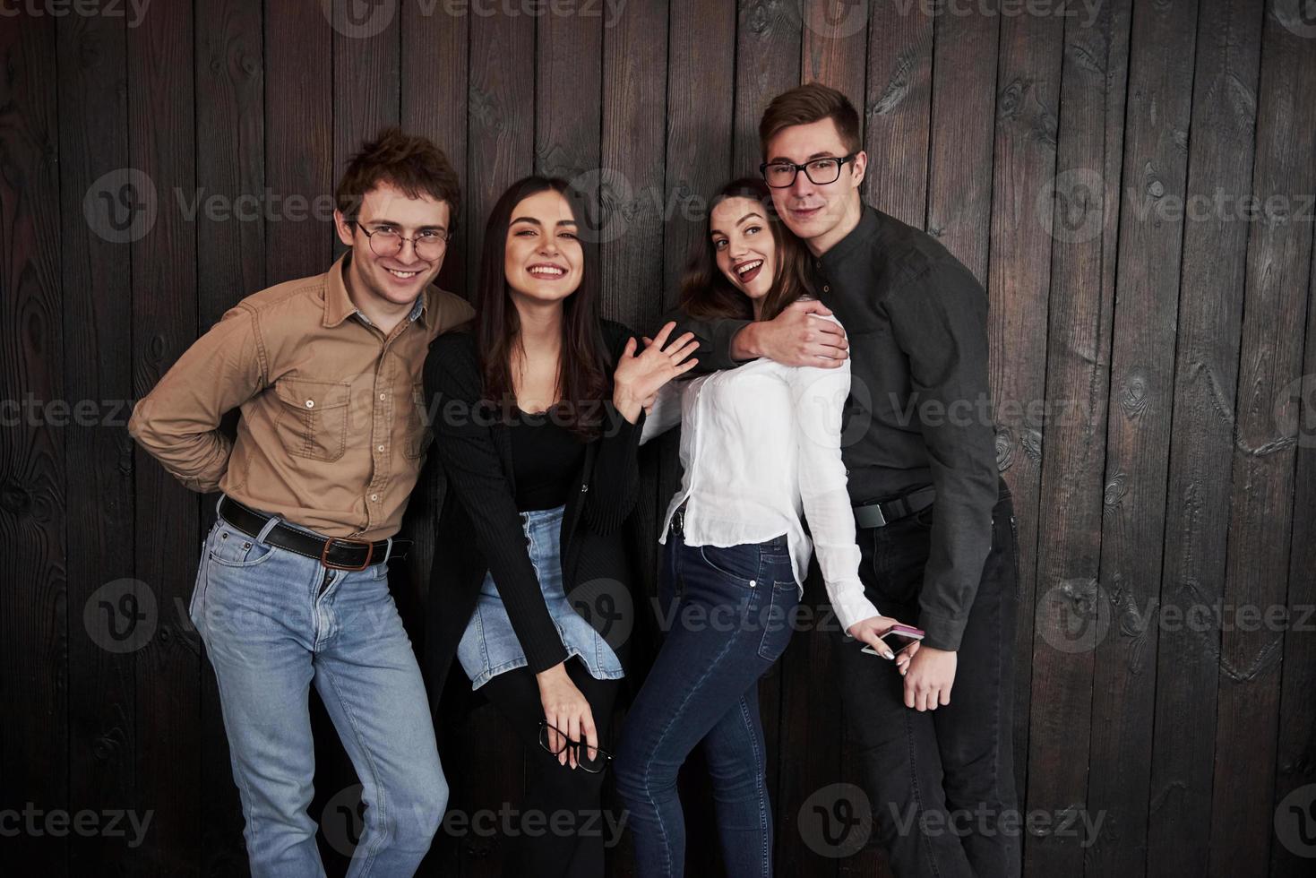 vier medewerkers hebben pauze. jeugd staat tegen zwarte houten muur. groep vrienden die samen tijd doorbrengen foto