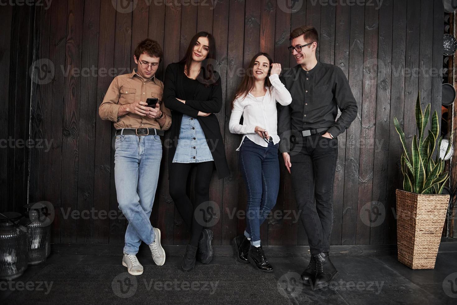 mooie schone kamer met plant aan de rechterkant. jeugd staat tegen zwarte houten muur. groep vrienden die samen tijd doorbrengen foto