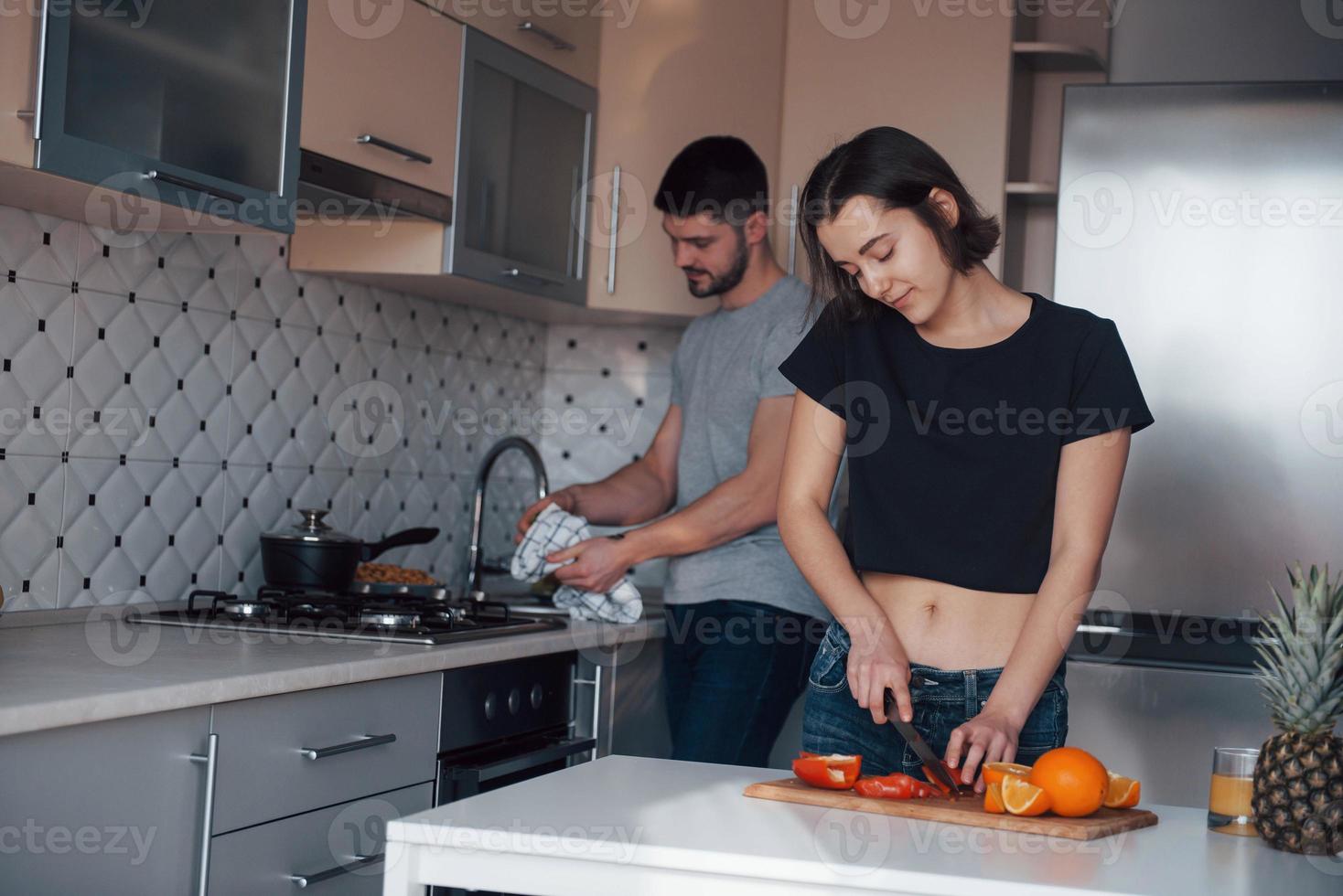 iedereen doet zijn werk. jong stel in de moderne keuken thuis in hun weekendtijd in de ochtend foto