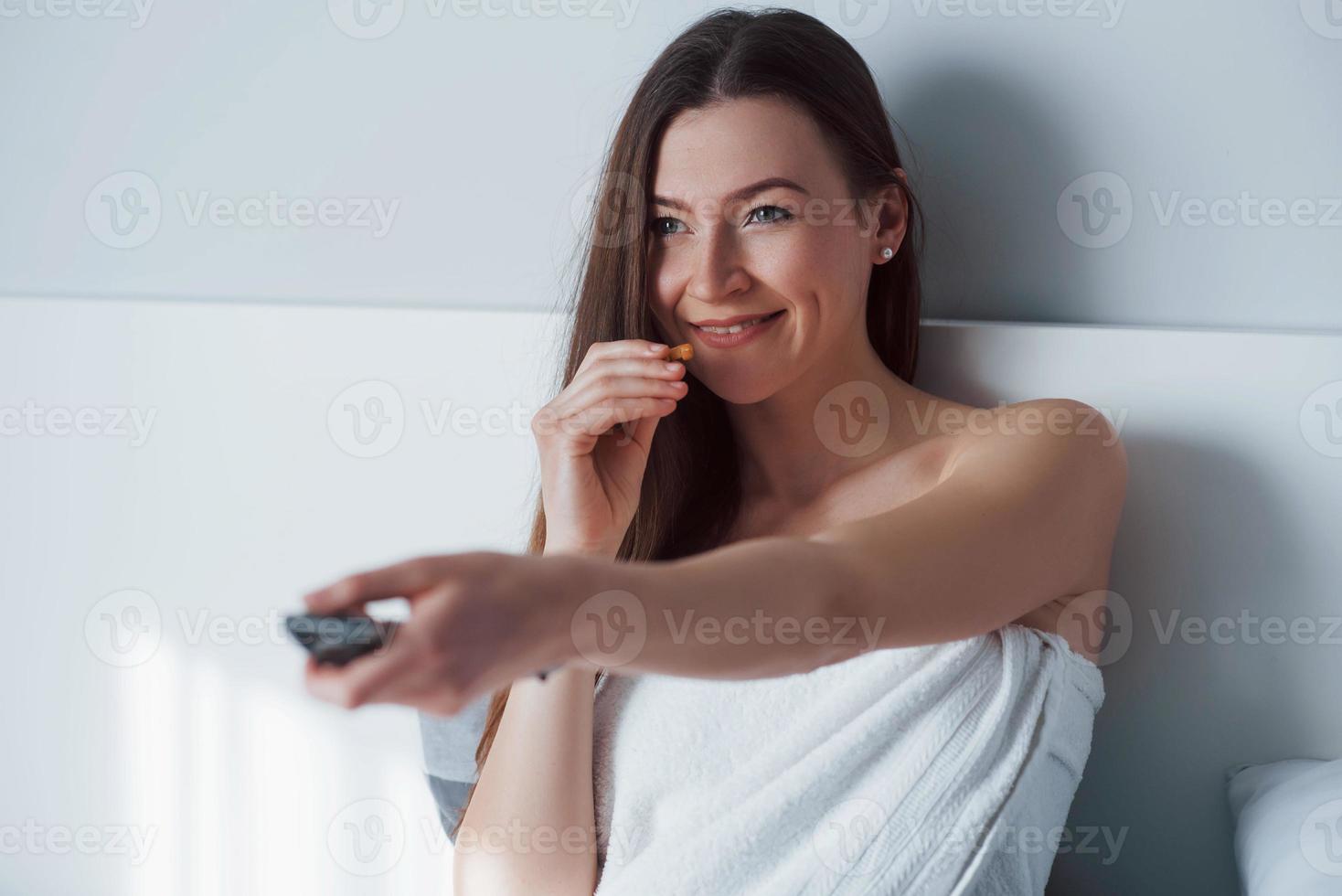 van kanaal wisselen. mooie jonge vrouw die 's ochtends in haar kamer op het bed zit foto