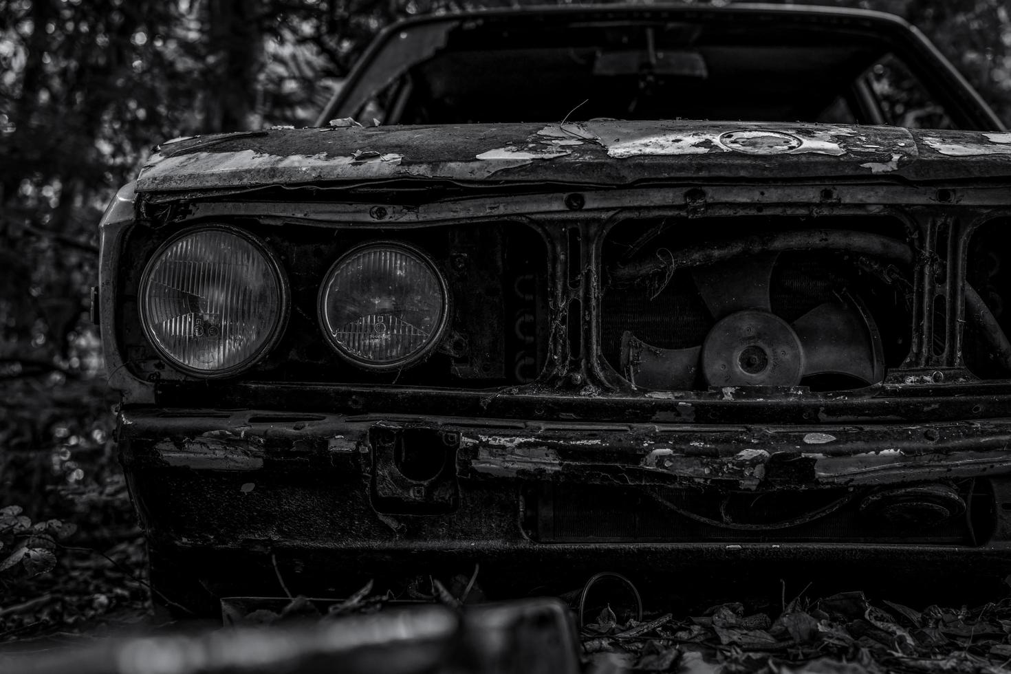 oude vernielde auto in zwart-wit scène. verlaten roestige auto in het bos. close-up vooraanzicht van rotte en roestige vernielde verlaten auto. de kunst van het verlaten van gebruikte auto's. tragedie en verlies. droefheid foto