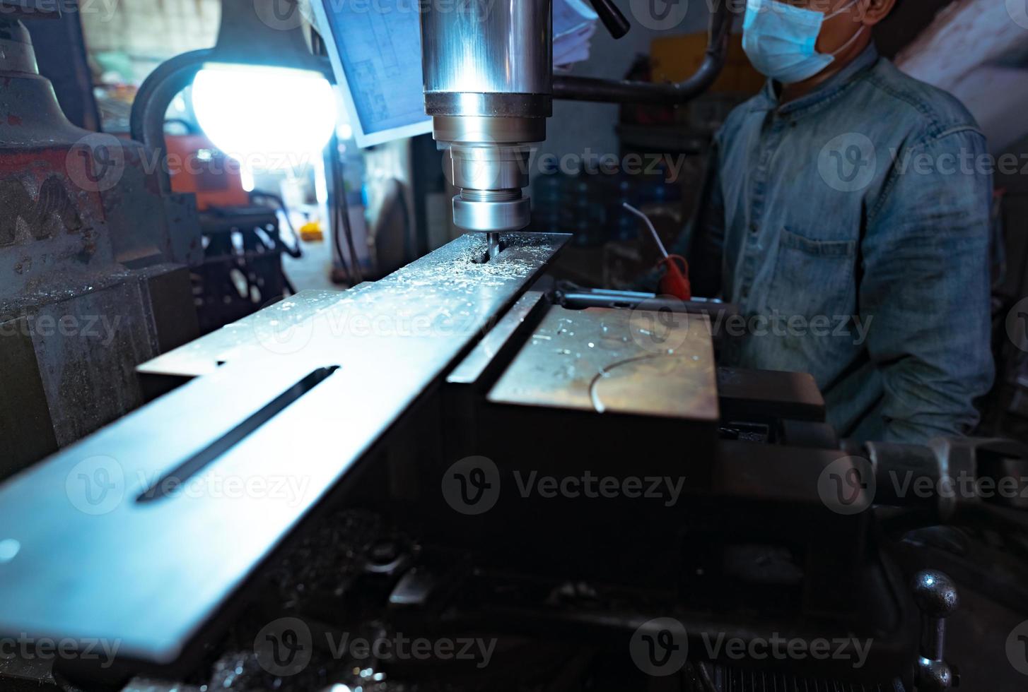 een man draagt een chirurgisch masker en werkt met een freesmachine. gereedschap voor gesneden metalen werkstuk. verticale freesmachine met hardmetalen frees. staalverwerkende industrie. maalproces. foto