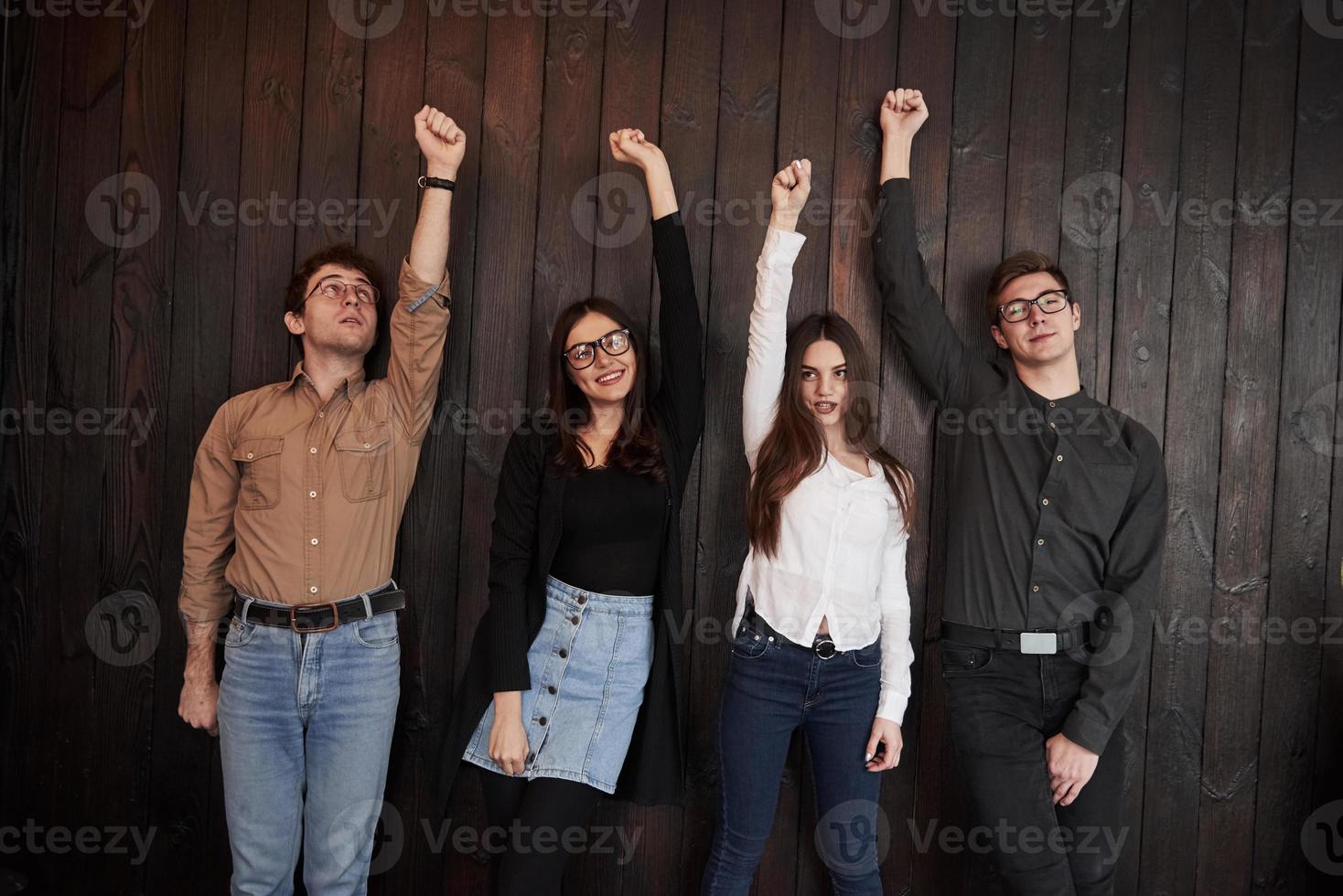 succes vieren. vrienden steken hun handen omhoog voor de zwarte houten muur foto
