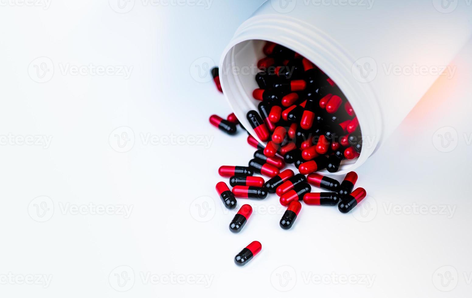 rode, zwarte capsules pil gemorst uit witte plastic fles container. resistentie tegen antibiotica. antimicrobiële capsulepillen. farmaceutische industrie. apotheek achtergrond. toxicologie van de geneeskunde foto