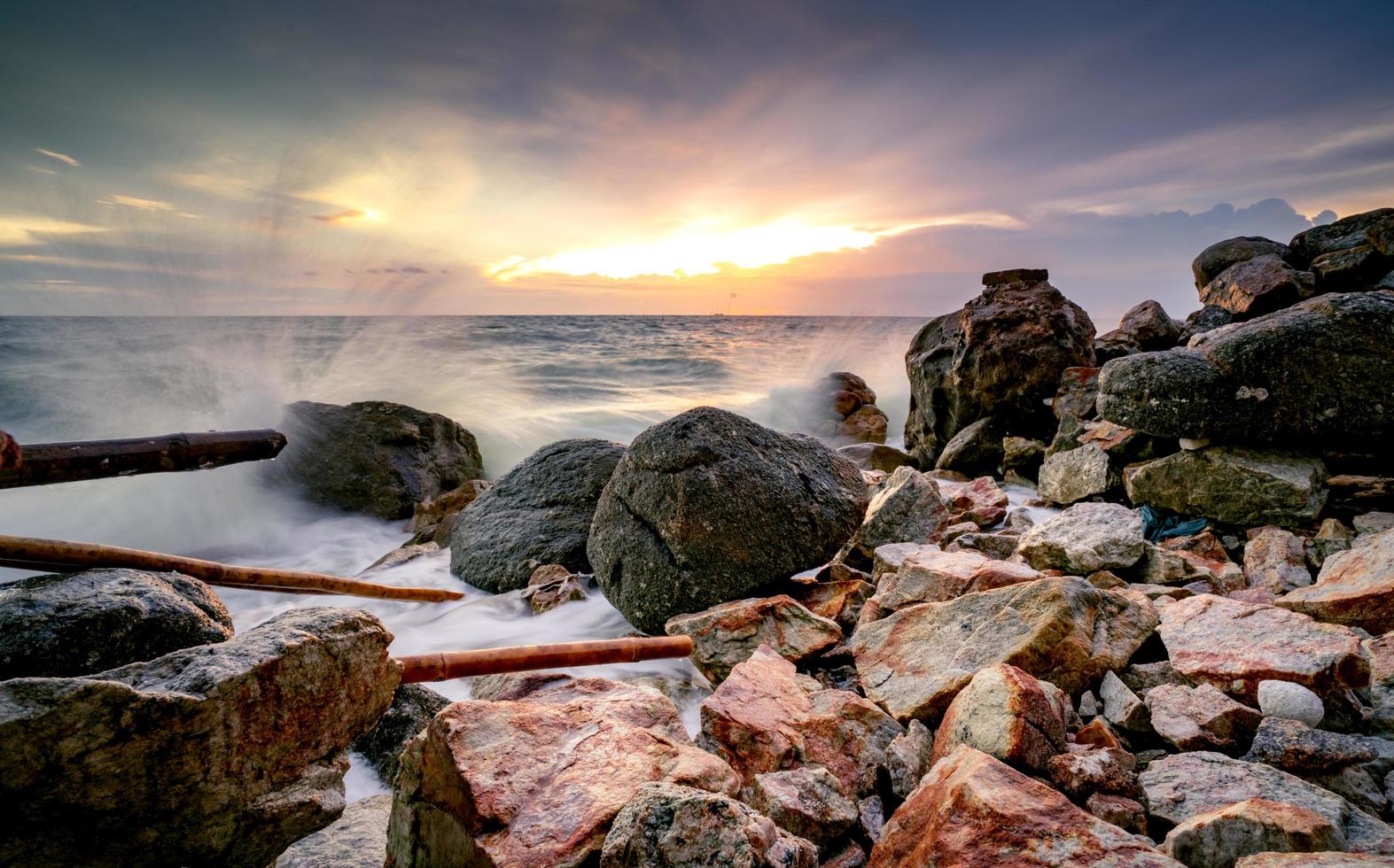 oceaanwaterplons op rotsstrand met mooie zonsonderganghemel en wolken. zee Golf spatten op steen op zee in de zomer. natuur landschap. tropisch paradijs strand bij zonsondergang. rotsstrand aan de kust. foto