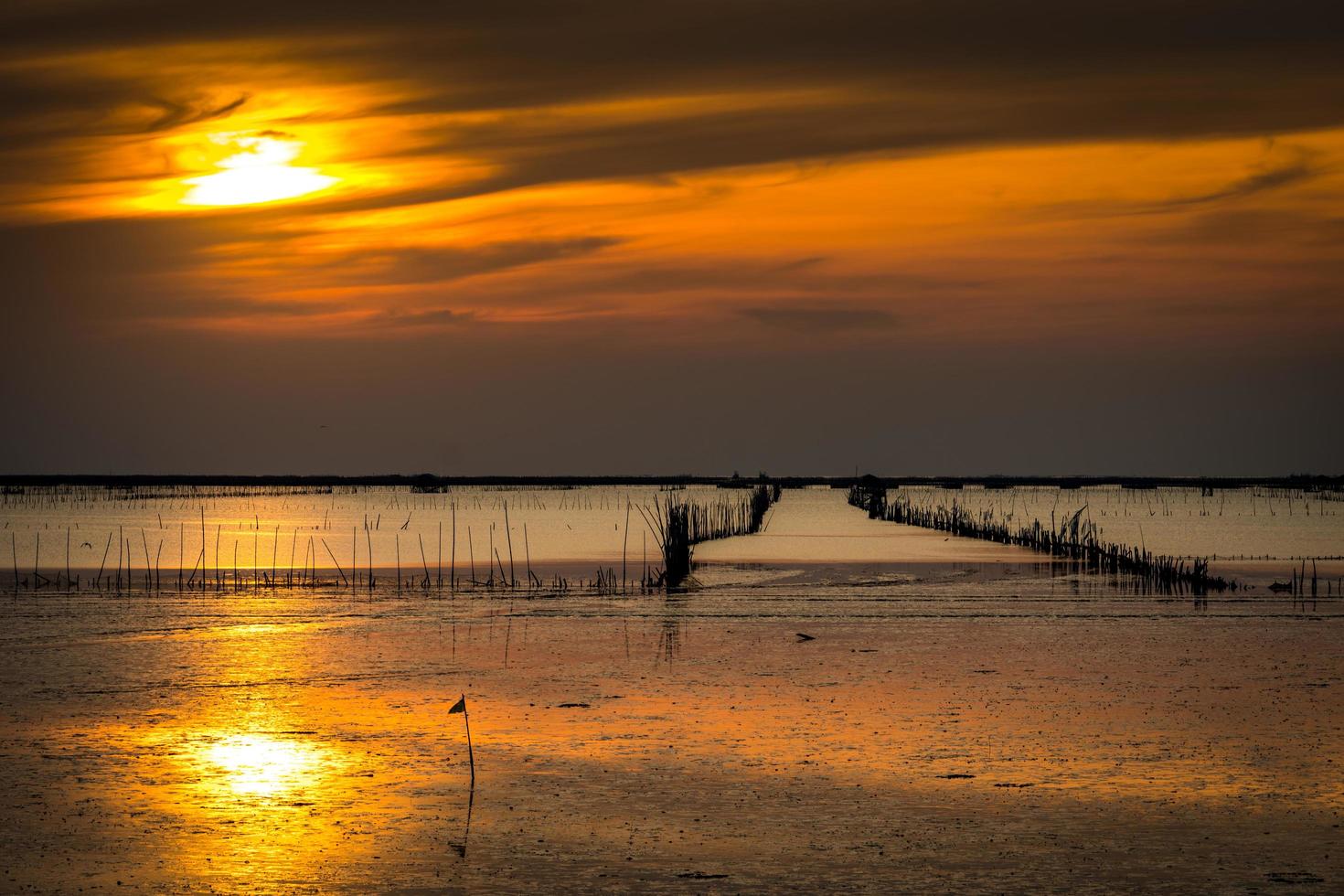 kust met laag waterpeil, schelpenboerderij met gedroogde bamboe en klei in de avond met oranje lucht en wolken. prachtige zonsondergang in tropische zee. foto