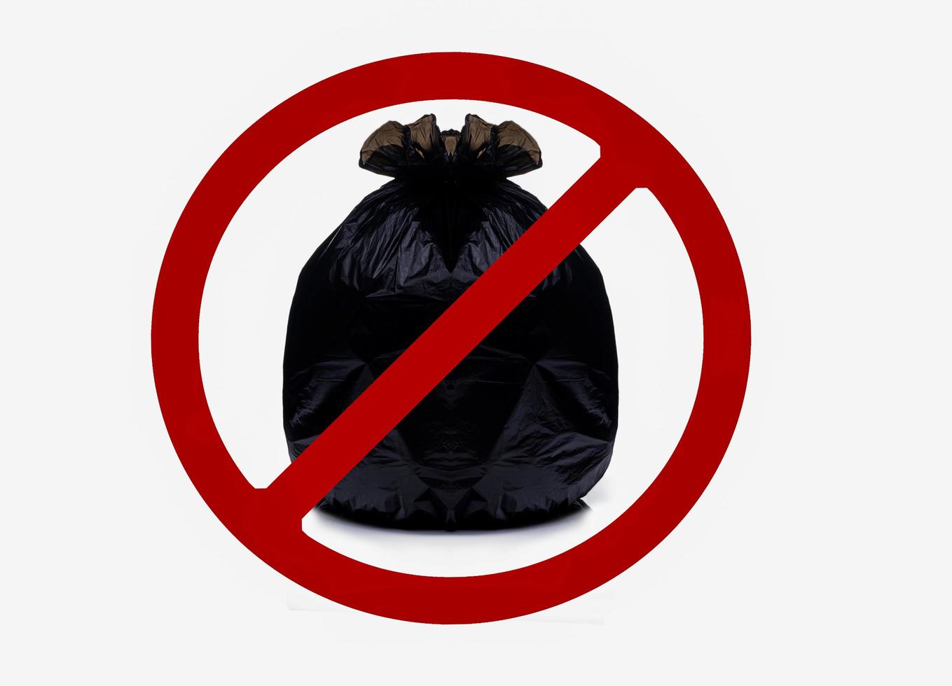 zwarte plastic zak bevat vol afval en bind de zak vast met een rood verboden bord. geen afval in dit gebied teken geïsoleerd op een witte achtergrond. zwarte plastic vuilniszak met gooi geen vuilnis hier bord. foto