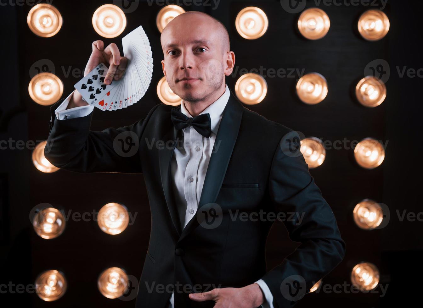 circusconcept. goochelaar in zwart pak en met speelkaarten in de kamer met speciale verlichting achter de schermen foto