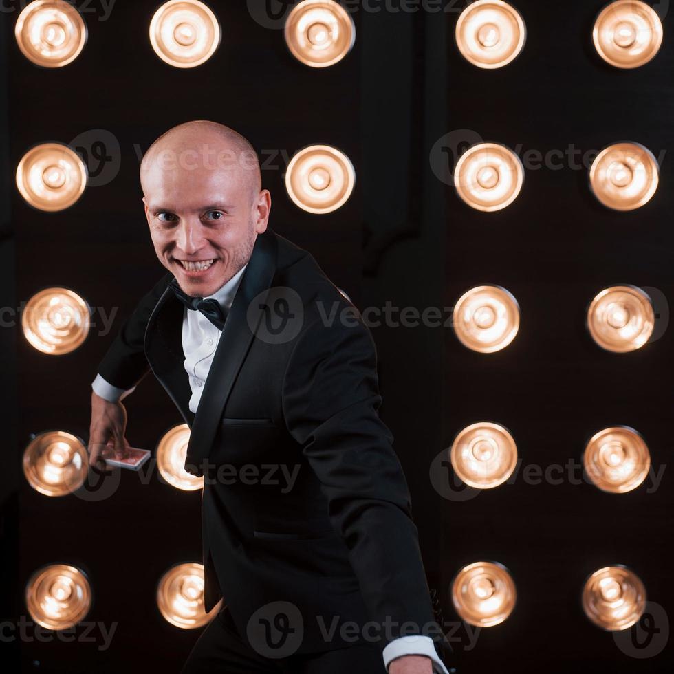 verticale foto. goochelaar in zwart pak staat in de kamer met speciale verlichting achter de schermen foto