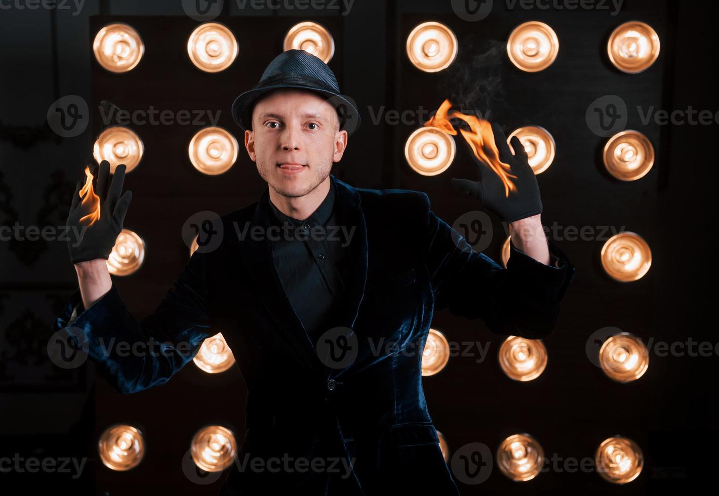 vooraanzicht. professionele illusionist in zwarte hoed, shirt en handschoenen spelen met vuur foto