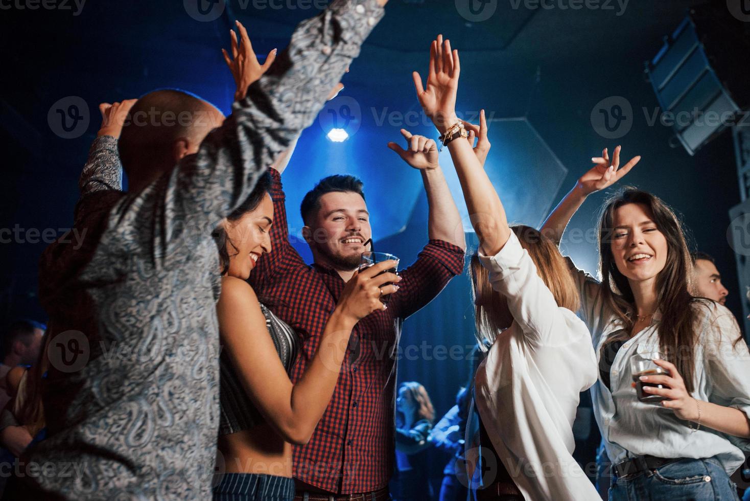 steek je handen in de lucht. gelukkige mensen dansen in de luxe nachtclub samen met verschillende drankjes in hun handen foto