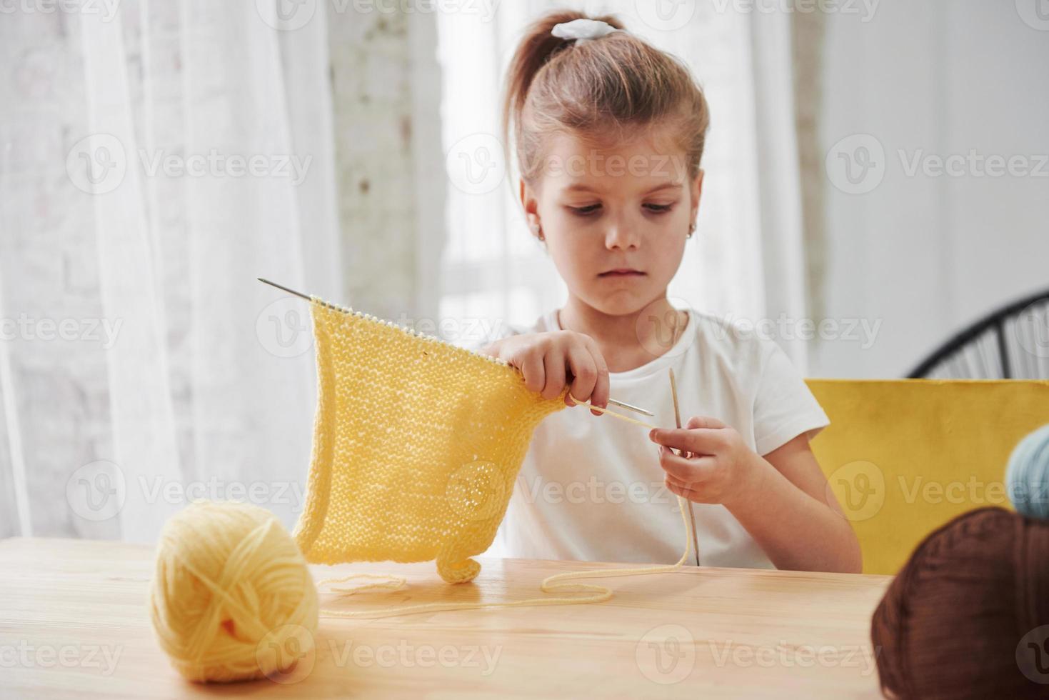ze is er goed in. kind breit thuis. schattig klein meisje dat bij de houten tafel zit, leert wat nieuwe dingen foto