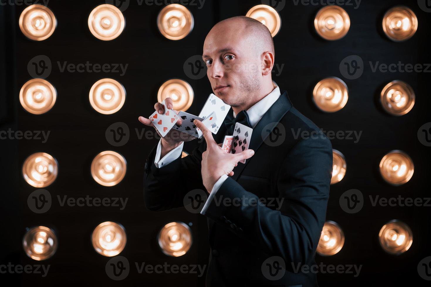 harde professionele trucs. goochelaar in zwart pak en met speelkaarten in de kamer met speciale verlichting achter de schermen foto