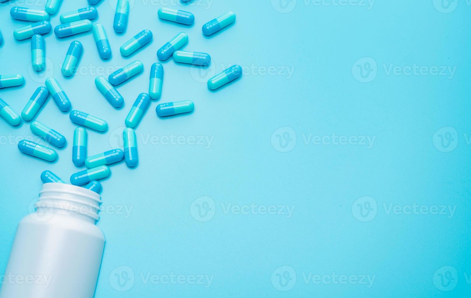 blauwe capsules pil gemorst uit witte plastic fles container op blauwe achtergrond met ruimte voor tekst. resistentie tegen antibiotica. antimicrobiële capsulepillen. farmaceutische industrie. apotheek. foto