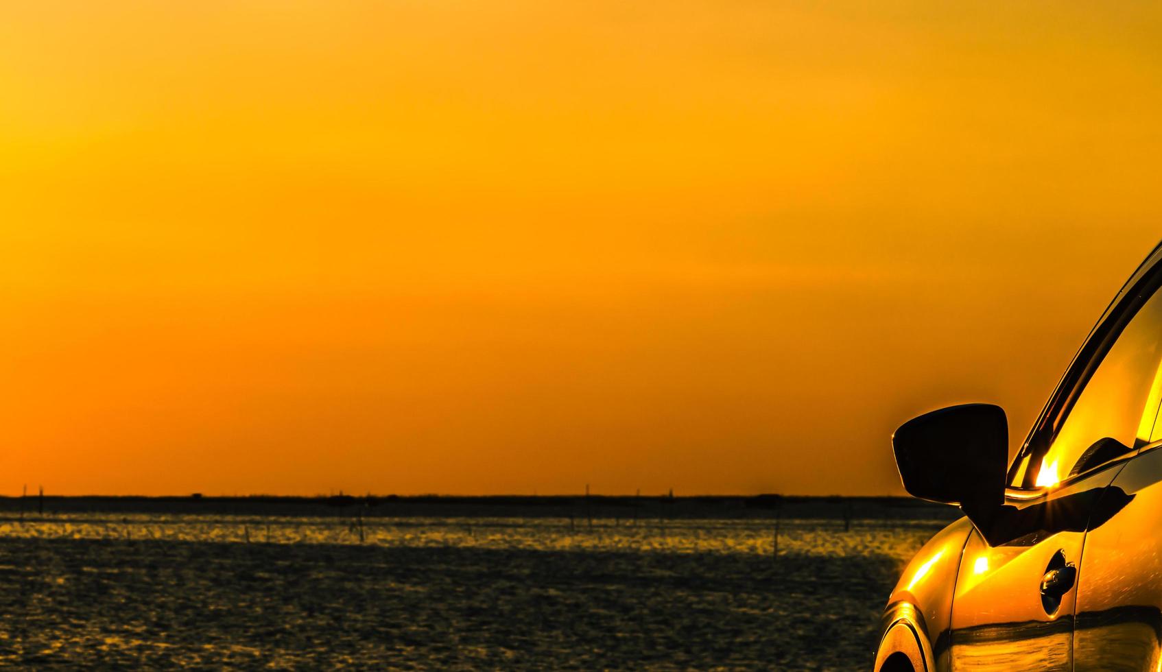 blauwe compacte suv-auto met sport en modern design geparkeerd op betonnen weg aan zee bij zonsondergang met oranje lucht. milieuvriendelijke technologie. zakelijk succesconcept. foto