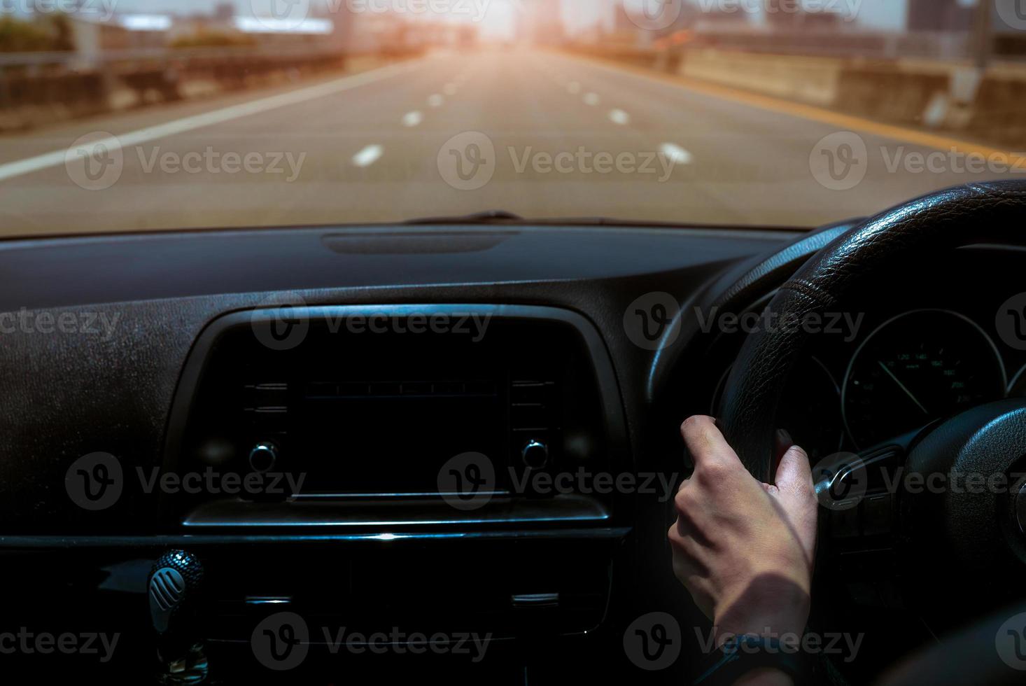 bestuurder hand met stuur voor controle auto. binnenaanzicht van de auto. dashboard en voorruit. auto rijden op betonnen weg in de stad. perspectief weergave auto op snelweg. bestuurder hand dragen slimme band foto