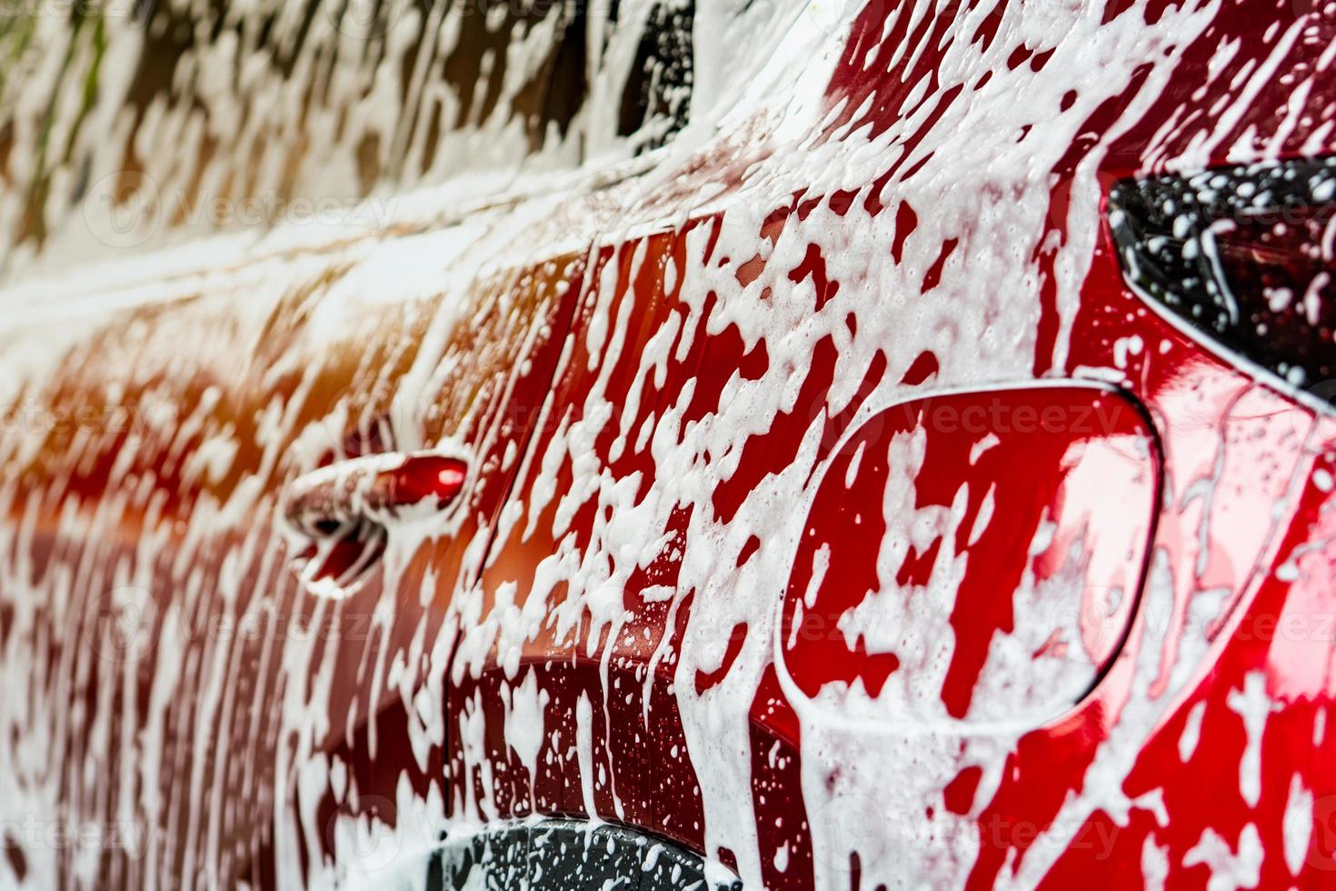 rode compacte suv-auto met sport en modern design wassen met zeep. auto bedekt met wit schuim. auto zorg service bedrijfsconcept. auto wassen met schuim voor glas waxen en glas coating auto. foto