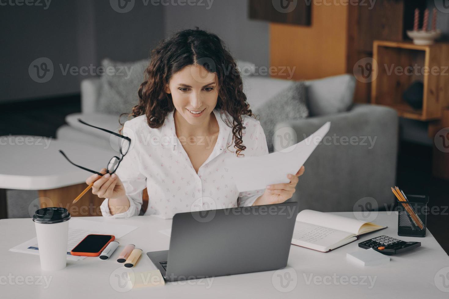 lachende blije italiaanse vrouw die thuis online rekeningen betaalt terwijl ze in de woonkamer zit foto