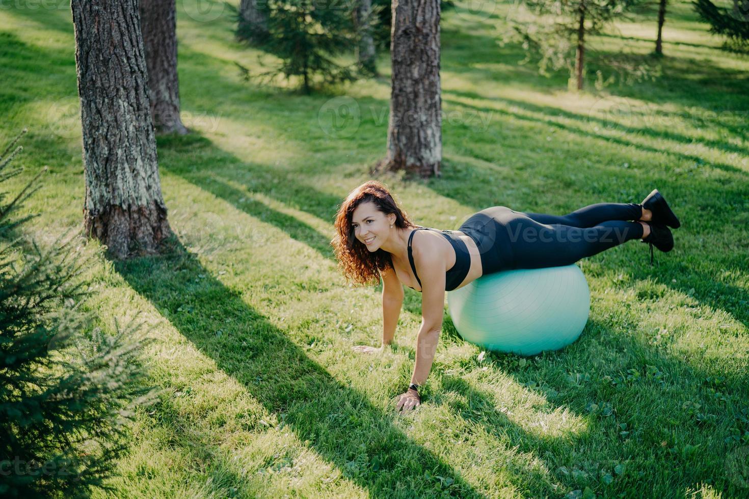 jonge tevreden sportieve vrouw doet fitnessoefeningen met fitnessbal, beoefent yoga in groen park of bos, is aerobicsinstructeur, blijft gezond en fit. lichamelijke activiteit en gymnastiek. foto