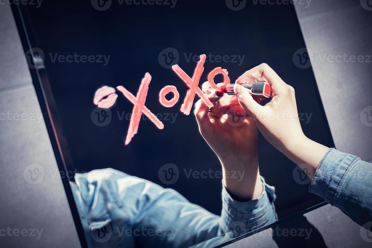 vrouw xoxo schrijven op een spiegel met rode lippenstift. foto