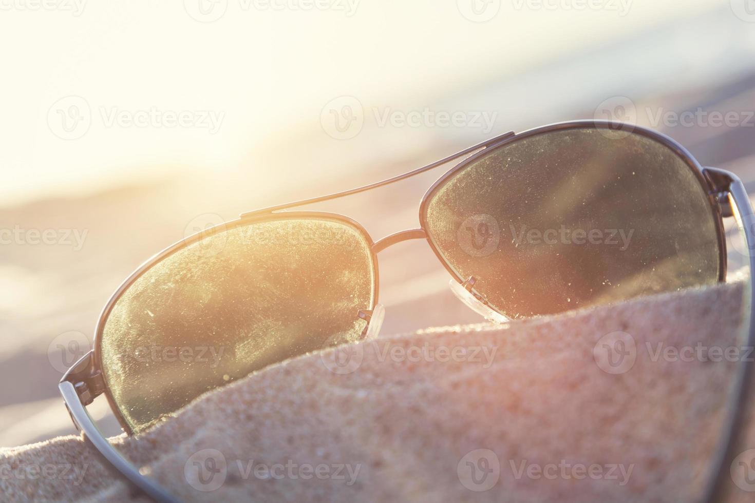 zonnebril op zand bij zonsondergang, strand en oceaan op de achtergrond. foto