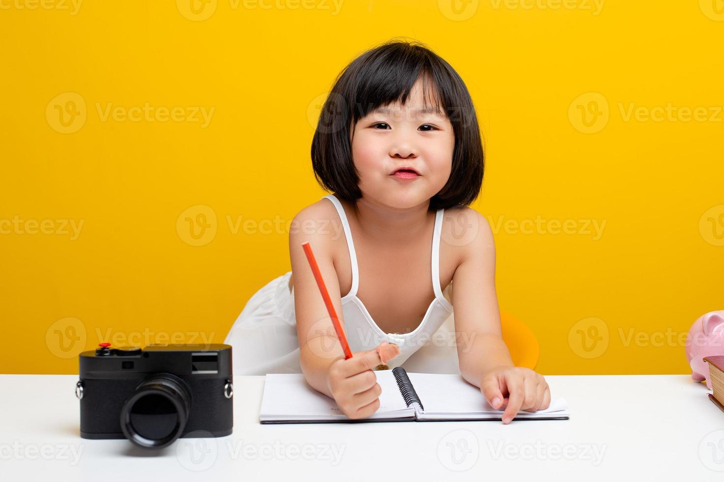 schattige meisjesfoto's azië schrijft een boek op kantoor voor hardwerkende kinderen. slimme kinderen. witte tafel op een gele achtergrond. foto