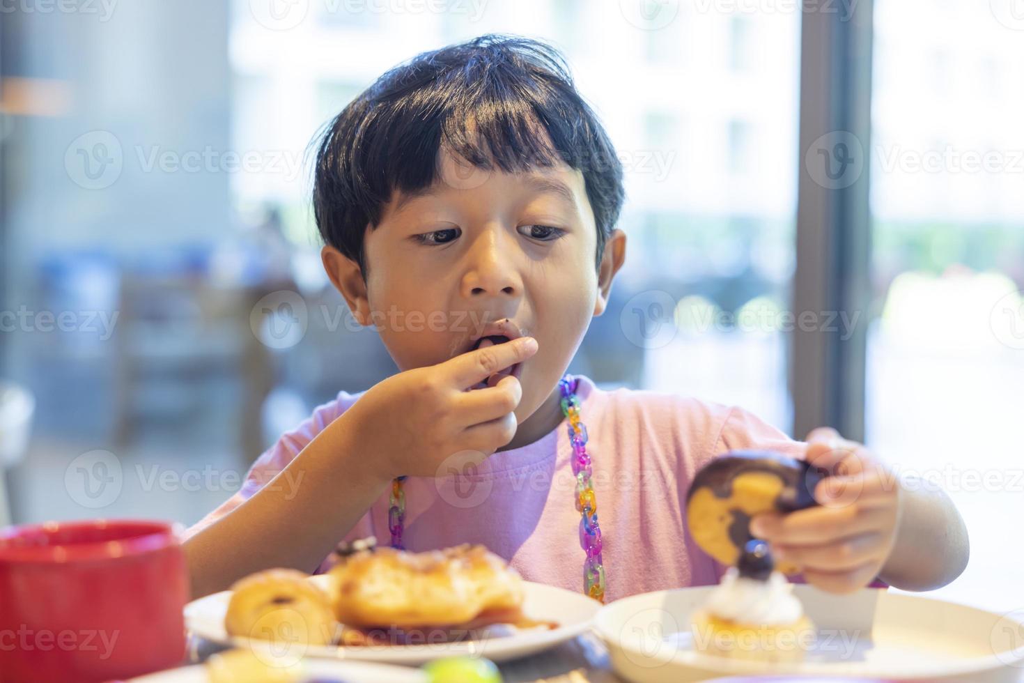 zwartharige Aziatische jongen in een roze shirt is blij met het ontbijt in het restaurant van het resortvakantie foto