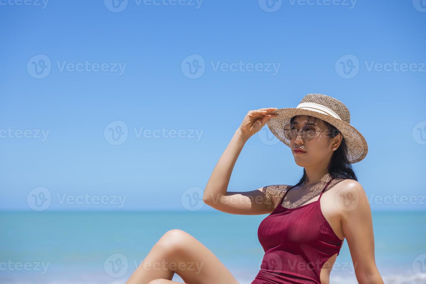 jonge vrouwen in bikini en strohoed zitten op tropisch strand en genieten van het uitzicht op de strandoceaan op een warme zomerdag. blauwe zee op de achtergrond. Khao Lak, Phang Nga, Thailand. zomervakantie concept foto