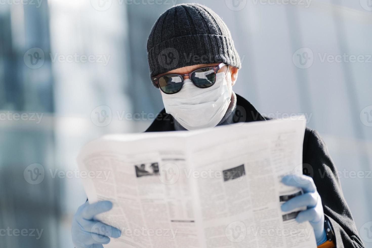 foto van europese man draagt beschermend medisch masker en handschoenen, loopt buiten door de stad, leest artikel over virusuitbraak in verschillende landen gebruikt beschermende maatregelen tijdens verspreiding van coronavirus