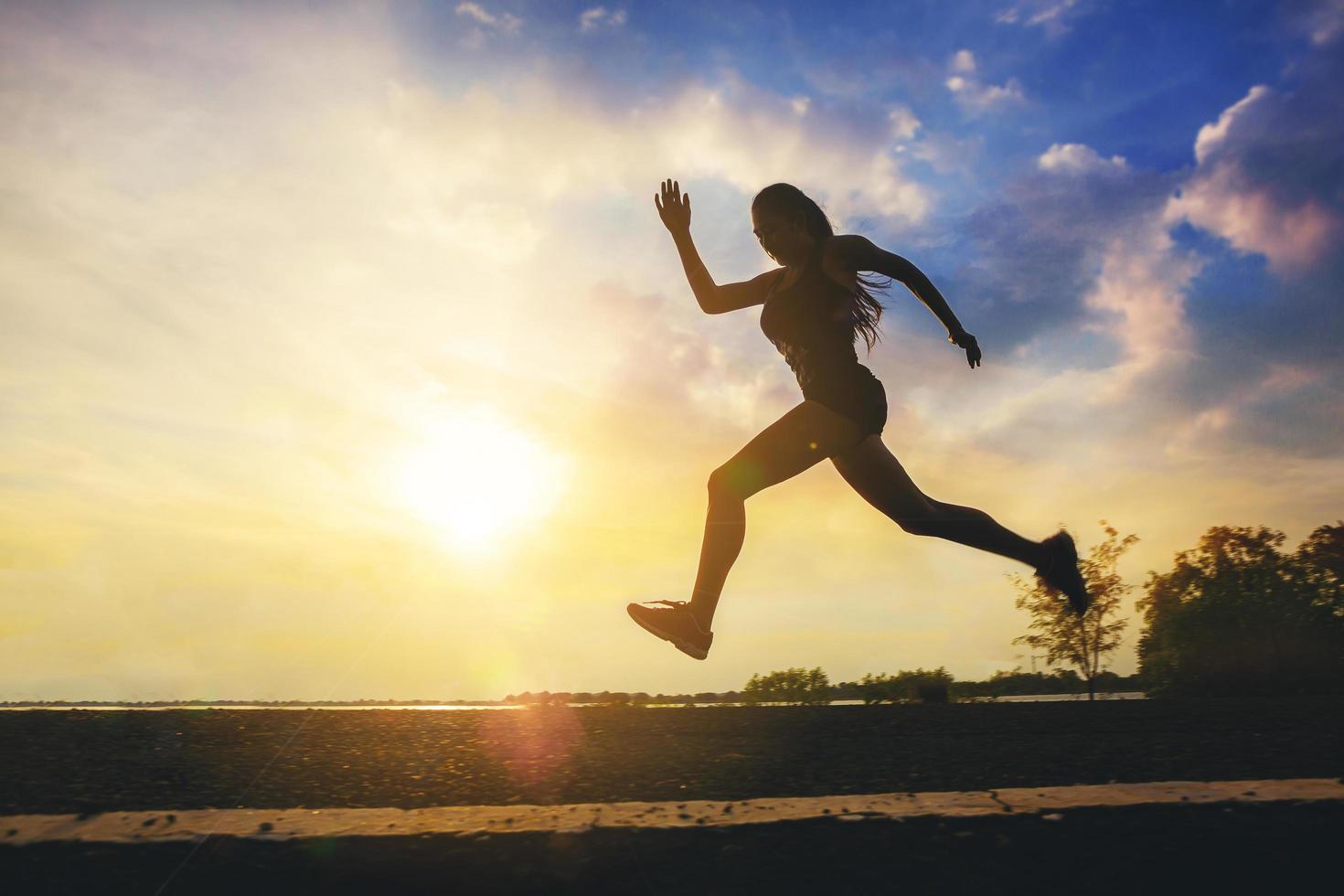 silhouet van jonge vrouw die sprinten op de weg loopt. fit runner fitness runner tijdens outdoor training met zonsondergang achtergrond. foto