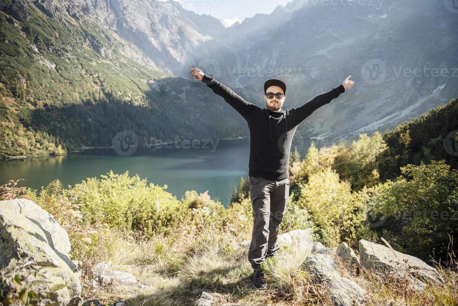 jonge toeristische man in een pet met handen omhoog op de top van de bergen foto