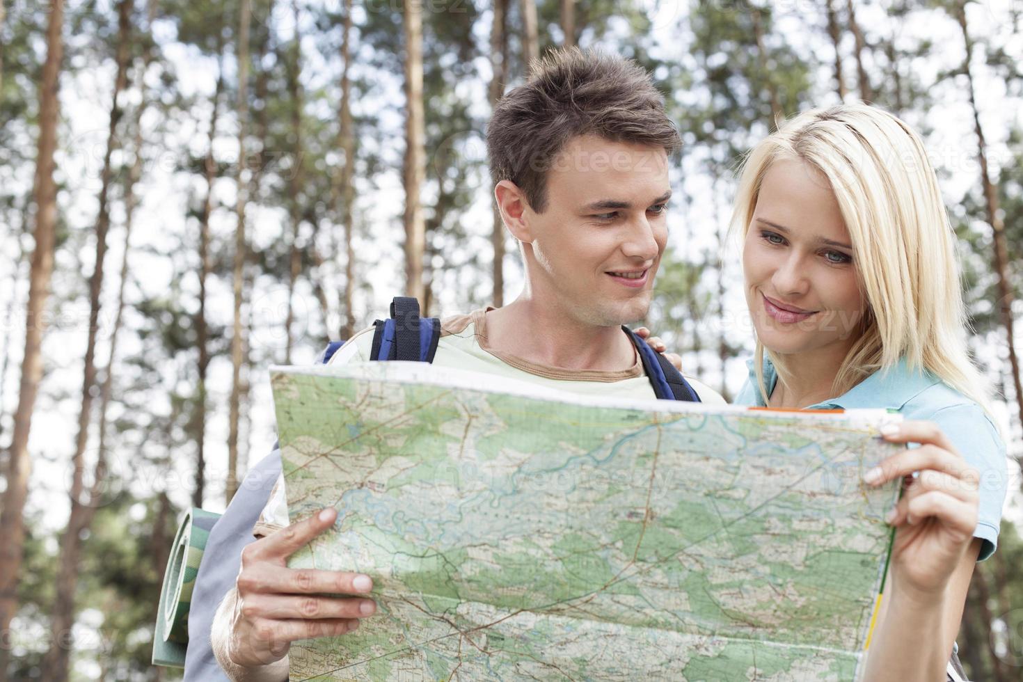gelukkige jonge backpackers die kaart in bos lezen foto