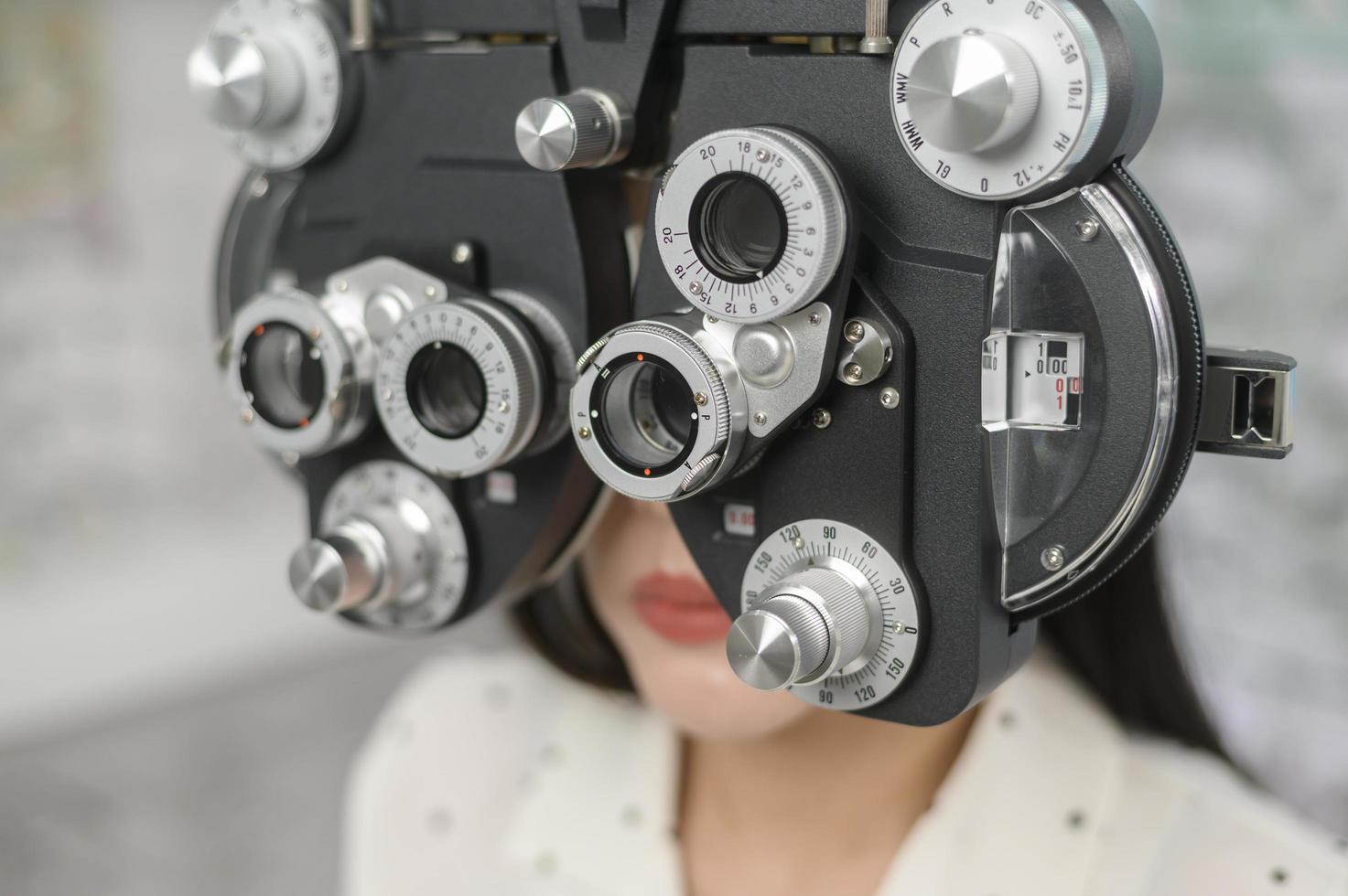 jonge vrouwelijke klant wordt onderzocht visuele test met behulp van bifocale optometrie gezichtsvermogen meetapparaat door oogarts in optisch centrum, oogzorg concept. foto