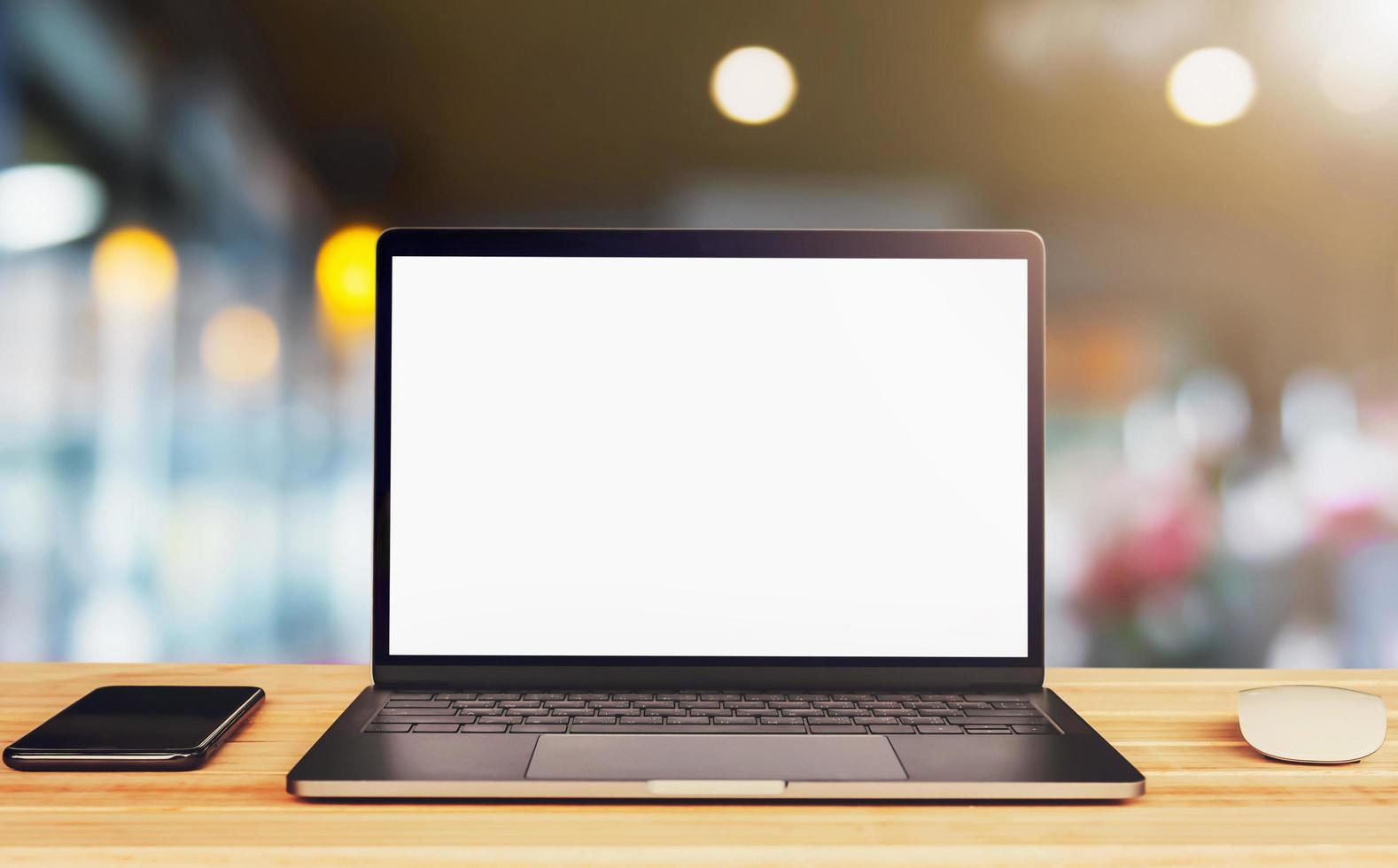 laptopcomputer leeg wit scherm en mobiel op tafel op caféachtergrond foto