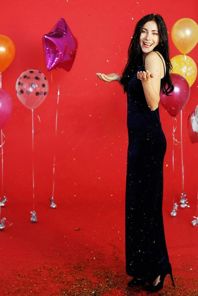 mooie vrouw lacht en danst in Kerstmis, verjaardag en viert oudejaarsavond met kleurrijke ballon op rode achtergrond foto