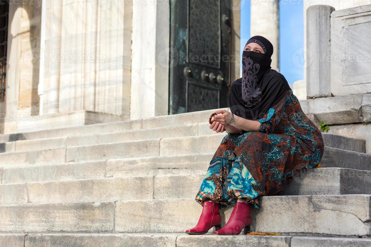 moslimstijl geklede dame die marmeren treden van blauwe moskee zit foto