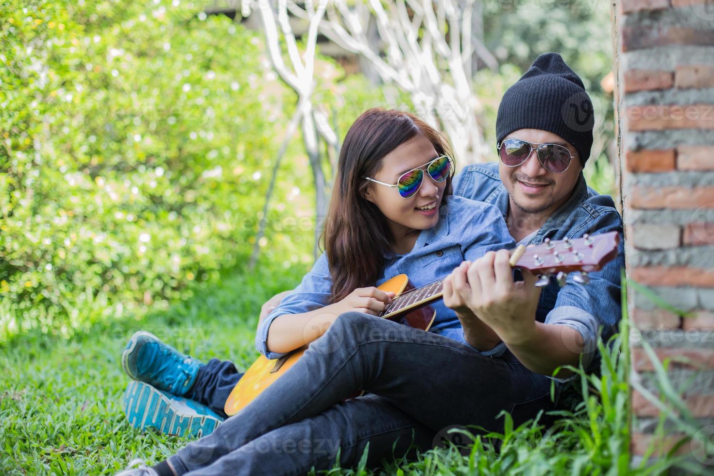 hipster man gitaar spelen voor zijn vriendin buiten tegen bakstenen muur, samen genieten. foto