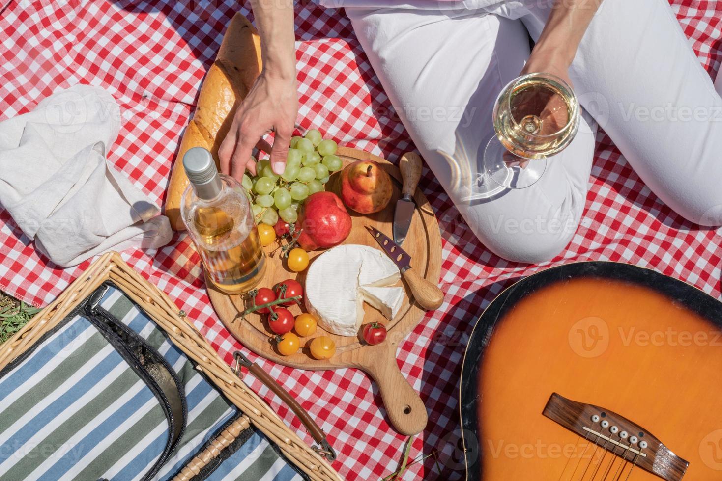 bovenaanzicht van onherkenbare jonge vrouw in witte broek buiten met picknick, eten en gitaar spelen foto