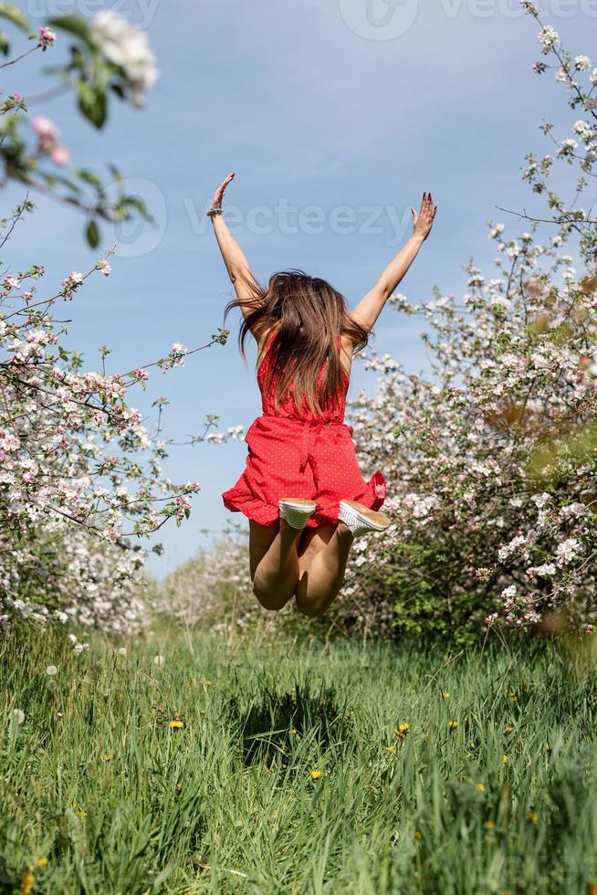 jonge blanke vrouw in rode jurk genieten van de bloei van een appelbomen, springen foto