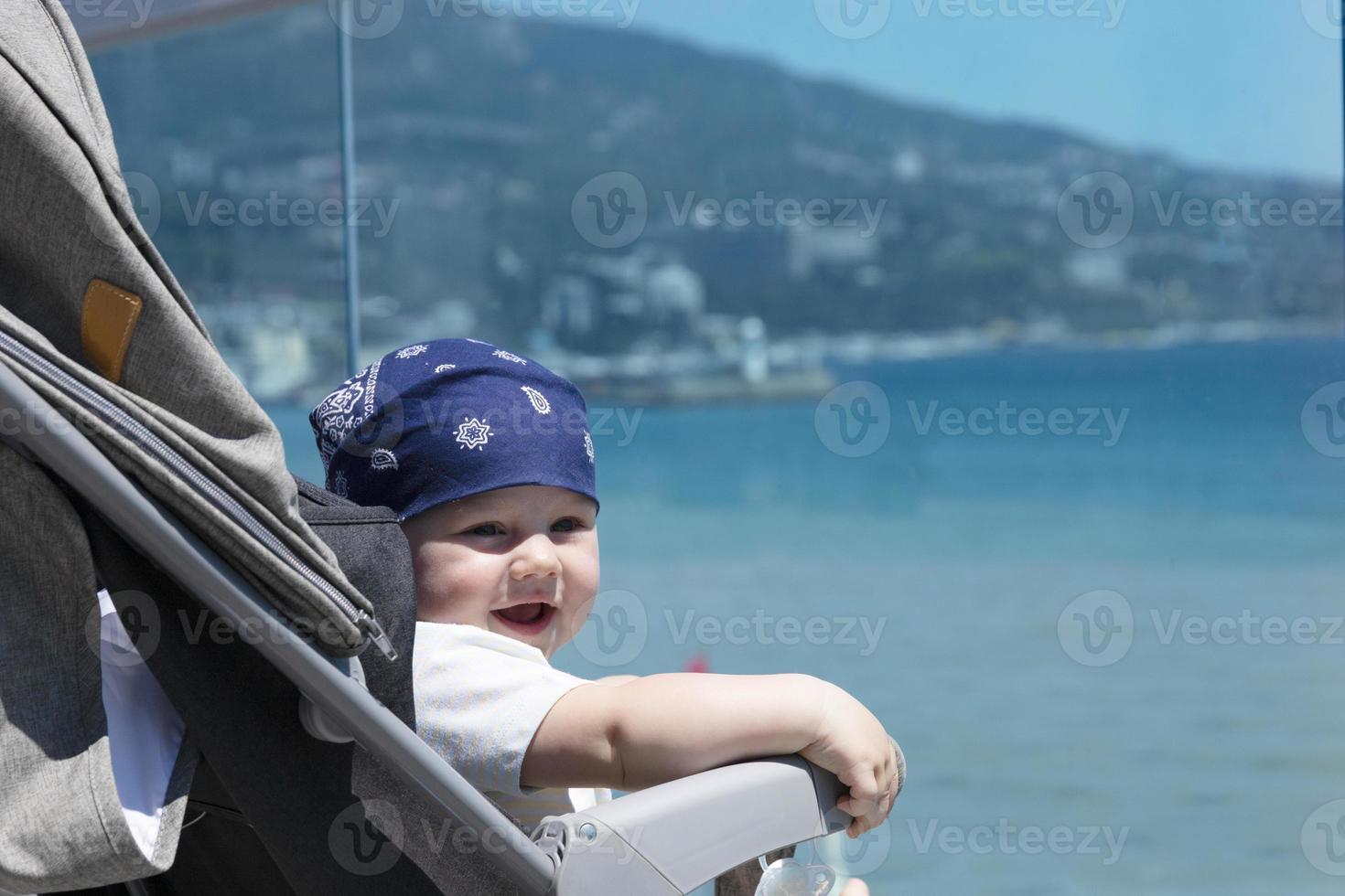 close-up van een schattige zeven maanden oude baby in een bandana die lacht tegen de achtergrond van de stadsdijk en de zee. foto