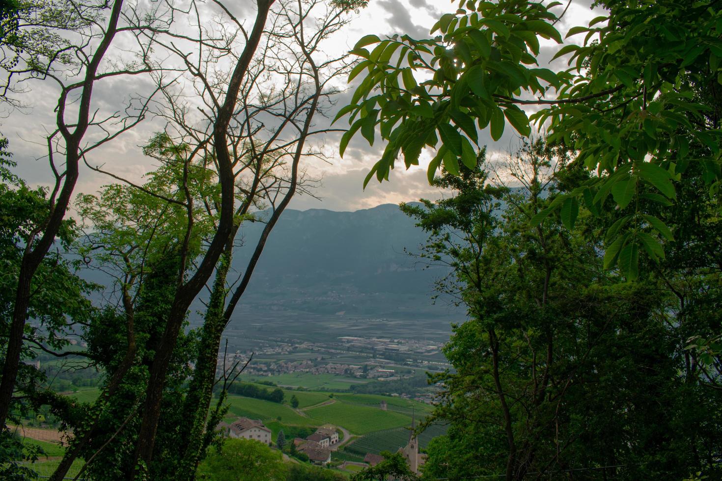landschap van landelijk dorp met bergen op de achtergrond, ingesloten in een frame van bomen foto