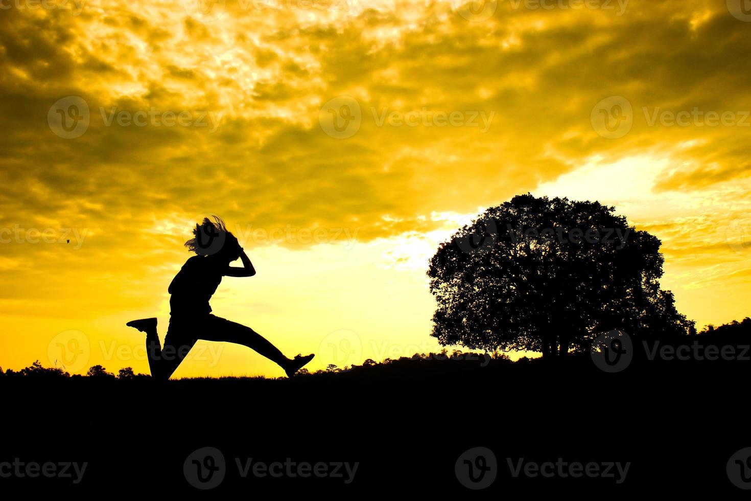 het silhouet van de vrouw die voor zonsopgang springt met een boom op de achtergrond foto