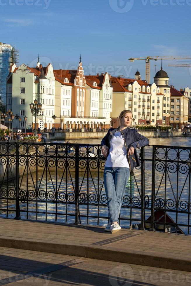 jonge blonde staat op de brug tegen de achtergrond van een prachtige stadsdijk foto