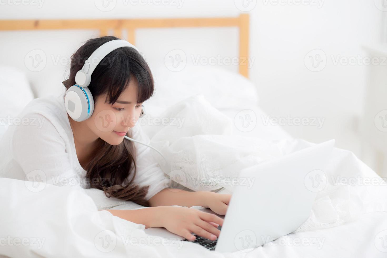 mooie jonge Aziatische vrouw liggend in de slaapkamer met behulp van laptopcomputer met video-oproep chat thuis, meisje begroeten en luisteren en praten messenger, communicatie en lifestyle concept. foto