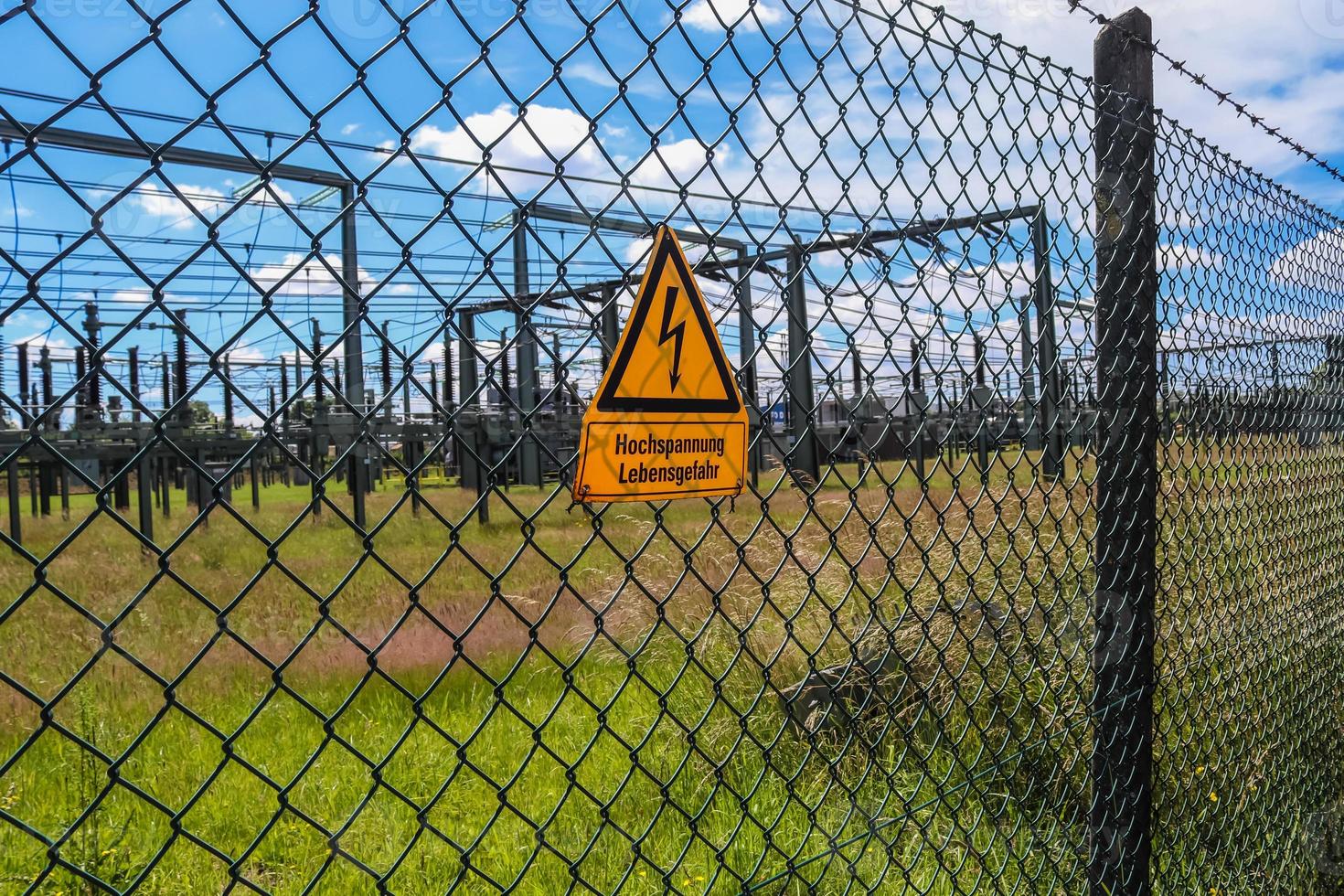bord met de woorden hoogspanning in de Duitse taal bij het hek van een groot onderstation dat elektrische energie distribueert met veel hoogspanningslijnen op een zonnige dag foto
