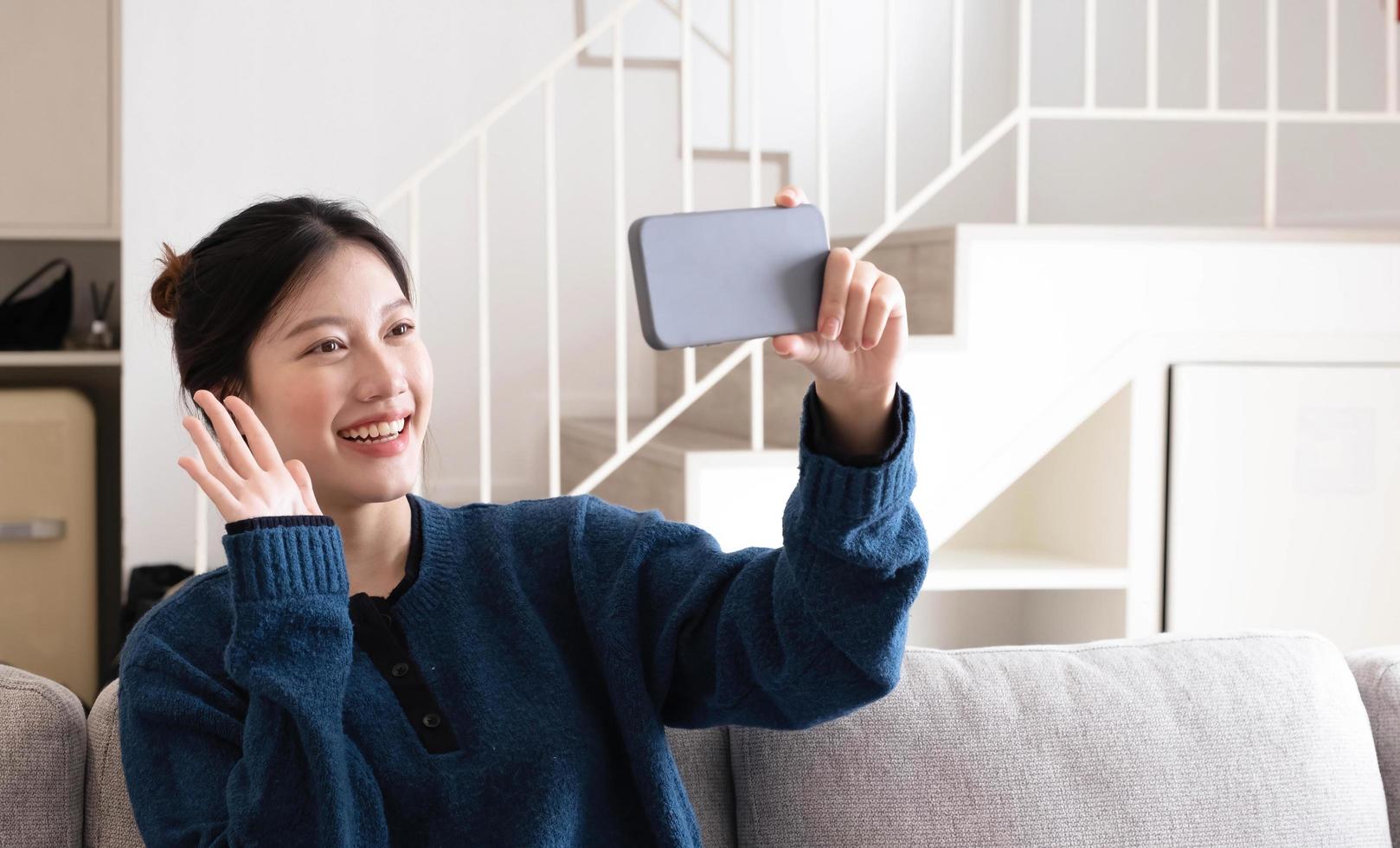 portret mooie jonge aziatische vrouw gebruikt slimme mobiele telefoon op de bank in het interieur van de woonkamer foto
